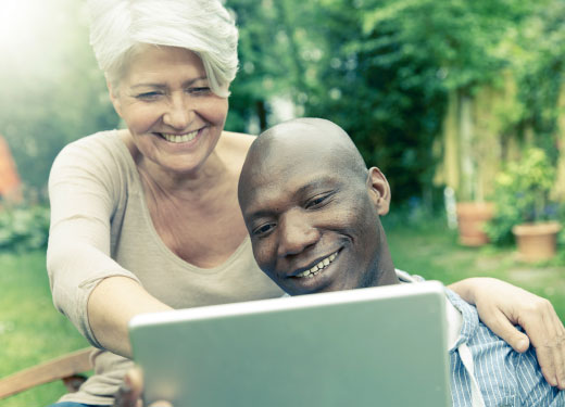 Eine Frau und ein junger Mann mit Migrationshintergrund schauen in ein Tablet: Beide lächeln.