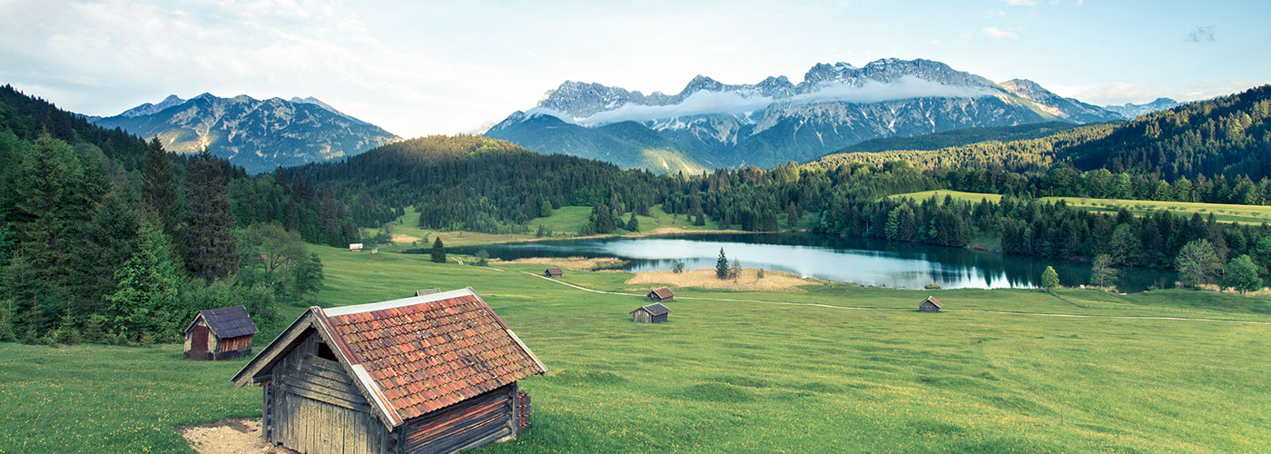 Landschaft in Bayern: Wiesen, Wälder und ein See. Dahinter die Berge.