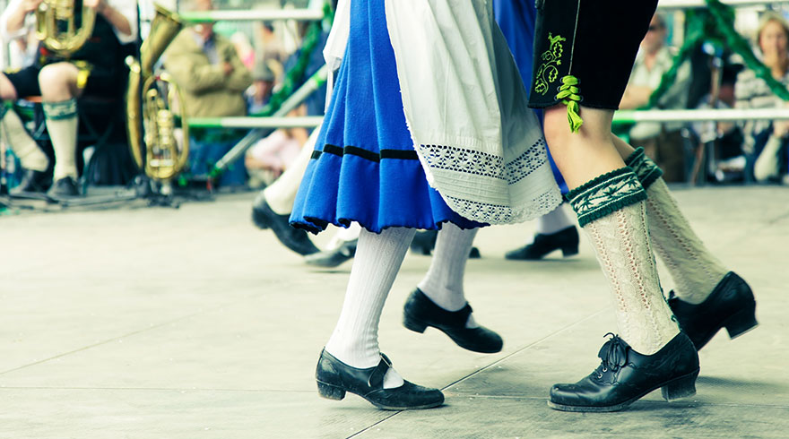 Close-up photo: the legs of men and woman dancing together at a festival. They are wearing traditional clothing.