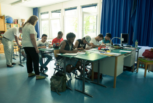 Unterrichtssituation: junge Migrantinnen und Migranten in einem Klassenzimmer.