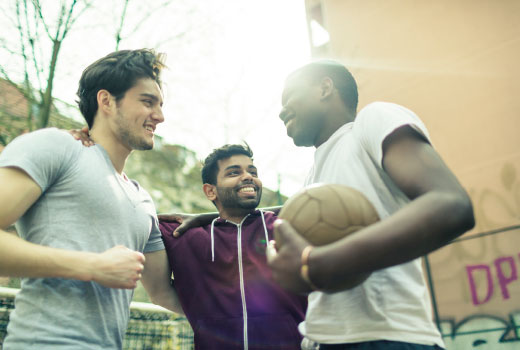 سه مرد جوان از ملیت های مختلف هنگام ورزش توپ. با خوشی همدیگر را حلقه زده اند.