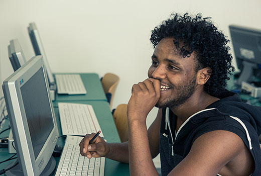 Tsegazgi Berhe sitzt am Computer. Er lächelt.