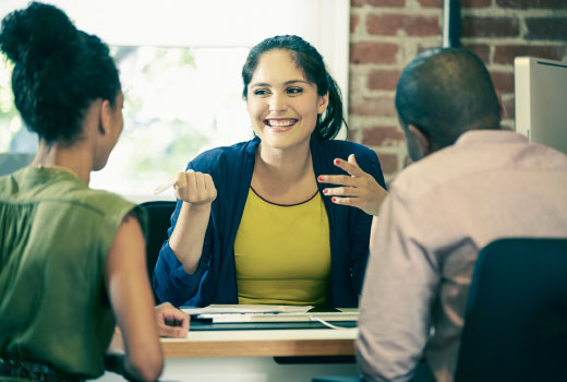 In conversation: a young woman and young man sit at a desk with a smiling woman.