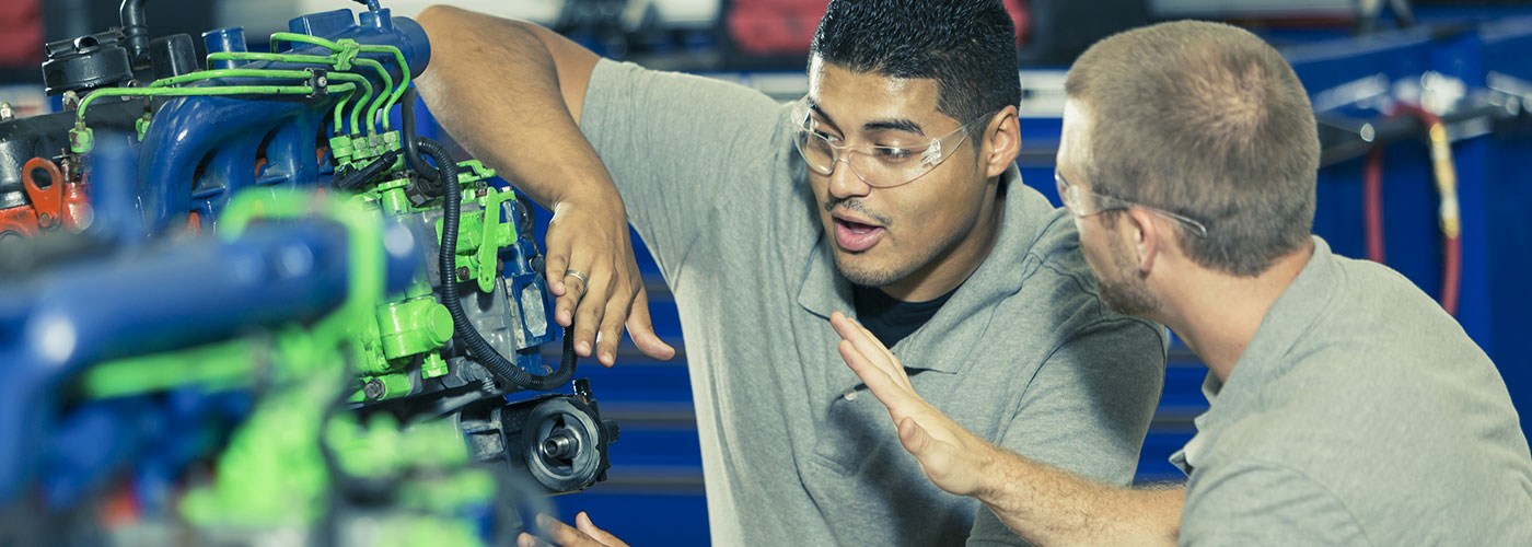 Two men, one from a migrant background, are inspecting an engine.