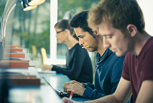 Three students sitting at a desk, concentrating on their work.